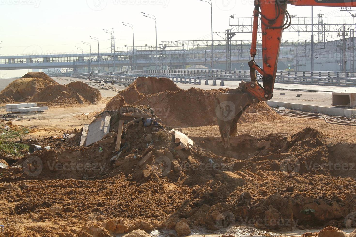 Excavator machinery working on construction site of new road to the city. Orange backhoe digs sand and gravel. Concept of renovation buildings, bridges and roads. Overpopulation problem. photo