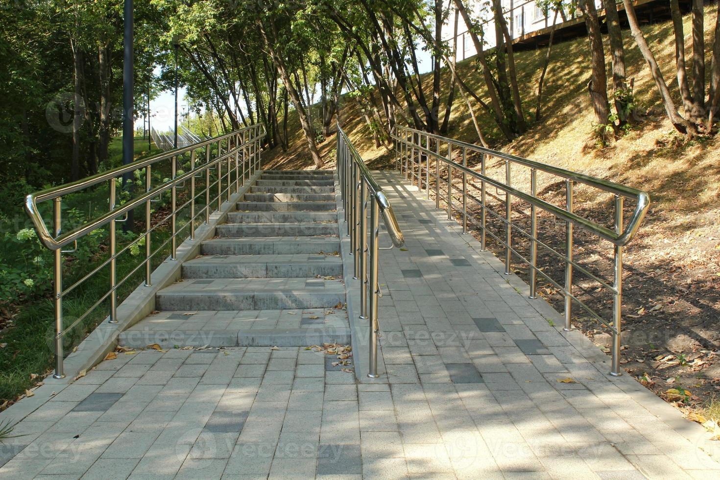 escaleras y rampa con barandillas metálicas para el paso de cochecitos y sillas de ruedas en parque público. concepto de entorno urbano cómodo y sin barreras en la ciudad. camino para personas con discapacidad foto