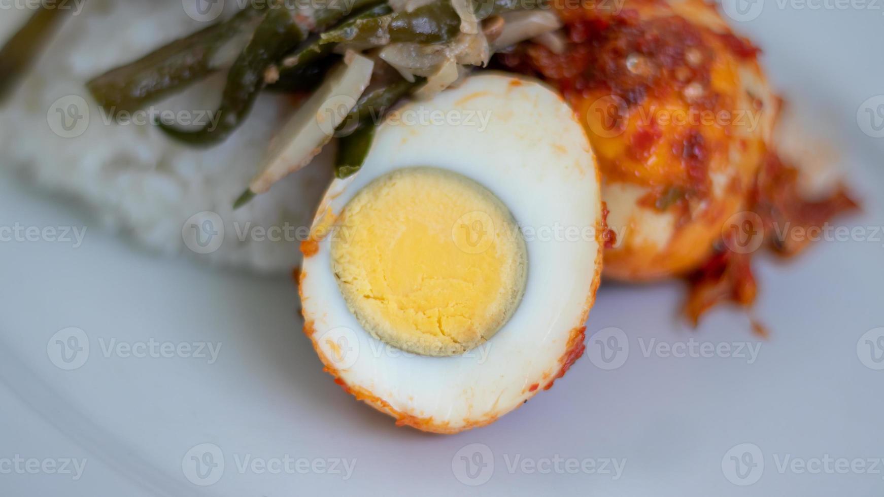 A plate of rice with egg balado and long bean sauce, chili sauce filled with eggs, anchovies and tofu. Served in a bowl on a gray background. Selected focus. photo