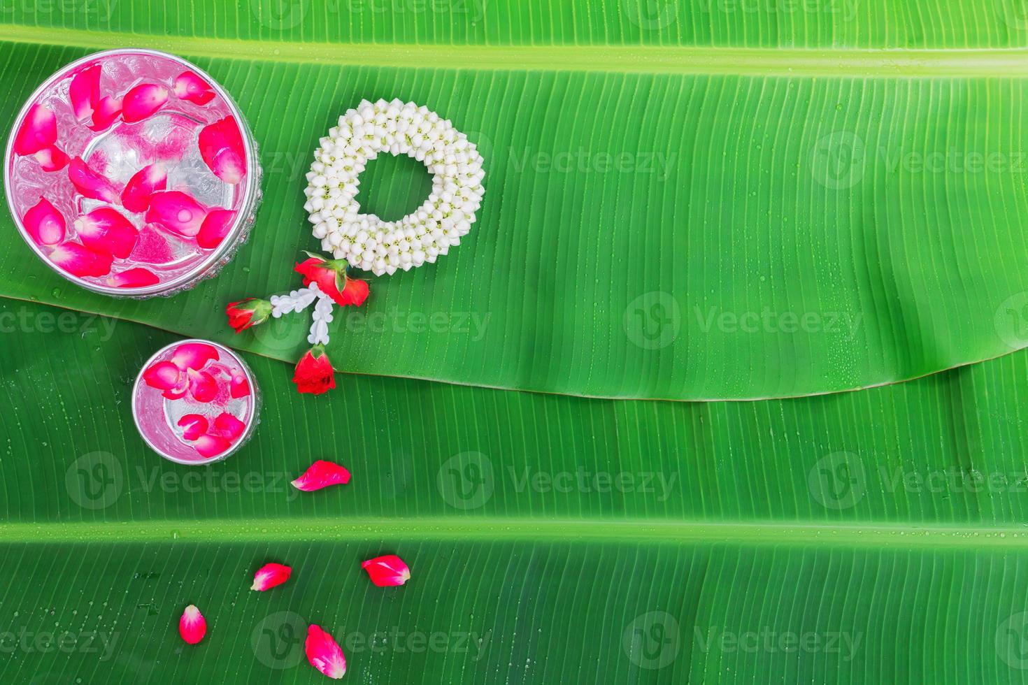 Songkran Festival background with jasmine garland Flowers in a bowl of water, perfume and limestone on a green wet banana leaf background. photo