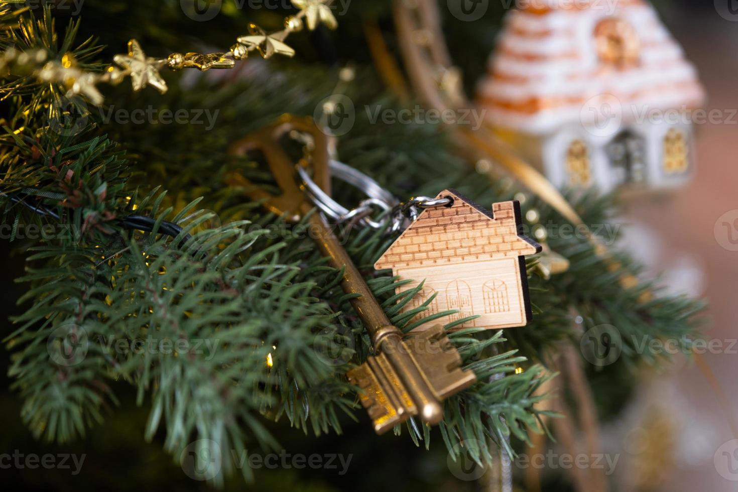 la llave de la casa con un llavero está colgada en el árbol de navidad. un regalo para año nuevo, navidad. construcción, diseño, proyecto, mudanza a casa nueva, hipoteca, alquiler y compra de bienes inmuebles. copie el espacio foto