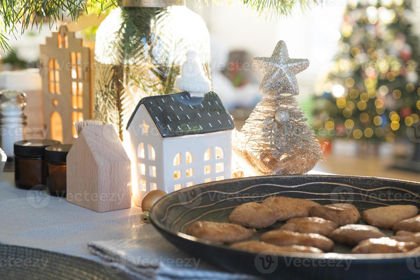 Festive Christmas decor in table, homemade cakes for breakfast, bakery cookies. Cozy home, christmas tree with fairy lights garlands. New Year, christmas mood photo