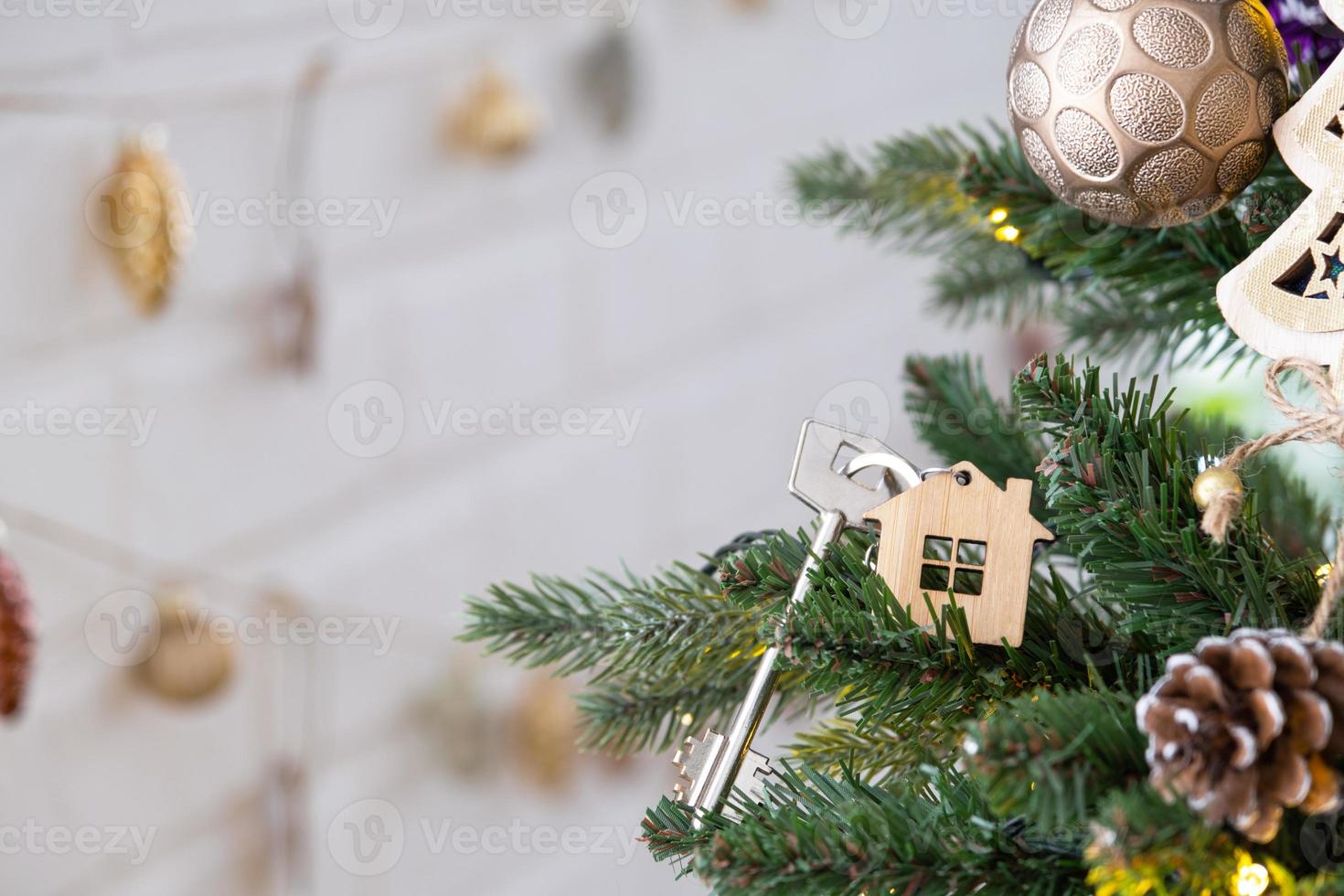 Key to the house with a keychain is hanging on the Christmas tree. A gift for New Year, Christmas. Building, design, project, moving to new house, mortgage, rent and purchase real estate. Copy space photo