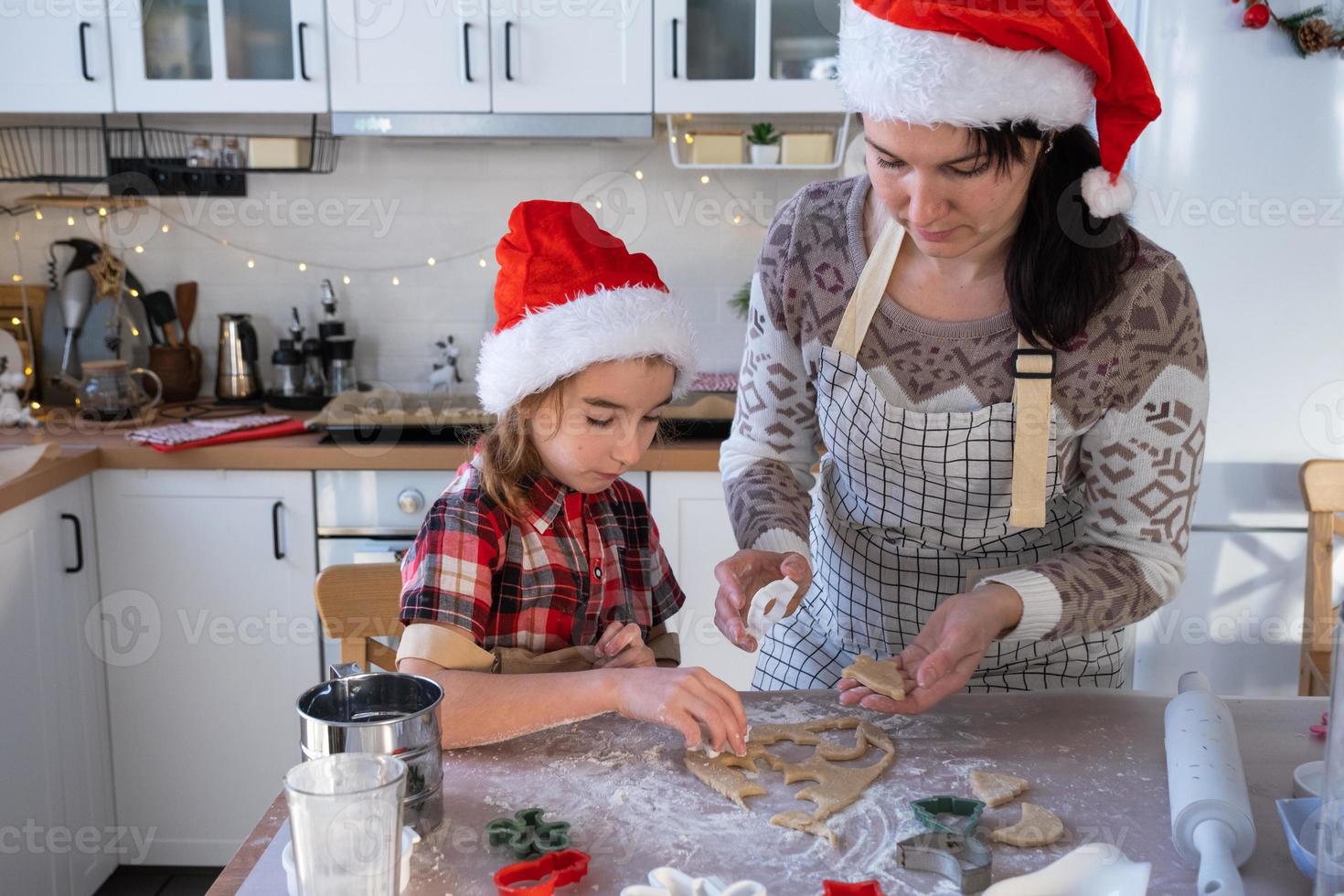 Mom and daughter in the white kitchen are preparing cookies for Christmas and new year. Family day, preparation for the holiday, learn to cook delicious pastries, cut shapes out of dough with molds photo