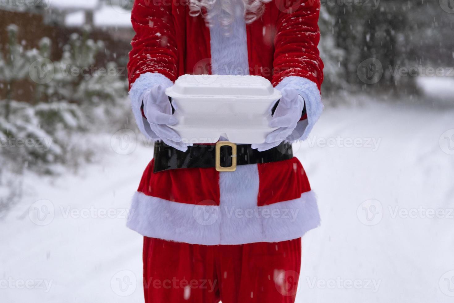 contenedores de servicio de entrega de alimentos en manos de santa claus al aire libre en la nieve. promoción de nochebuena. Pedido caliente listo para usar, caja de plástico desechable. catering de vacaciones de año nuevo. copia espacio, maqueta foto