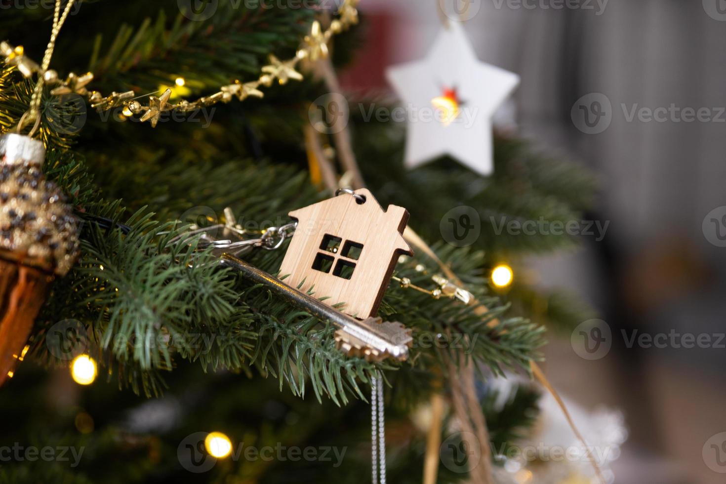 Key to the house with a keychain is hanging on the Christmas tree. A gift for New Year, Christmas. Building, design, project, moving to new house, mortgage, rent and purchase real estate. Copy space photo