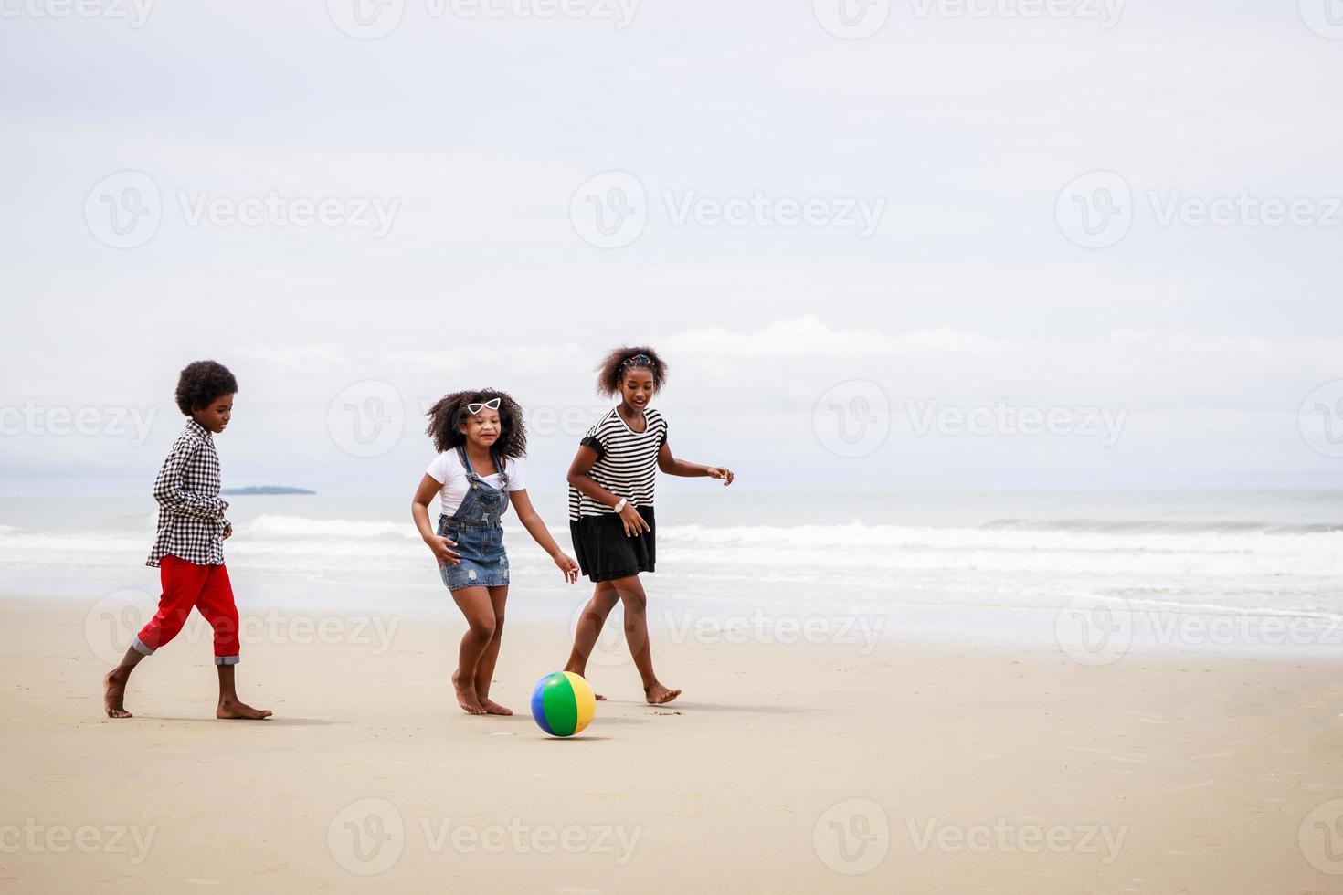 grupo de niños afroamericanos juegan a la pelota y se divierten en una playa tropical foto