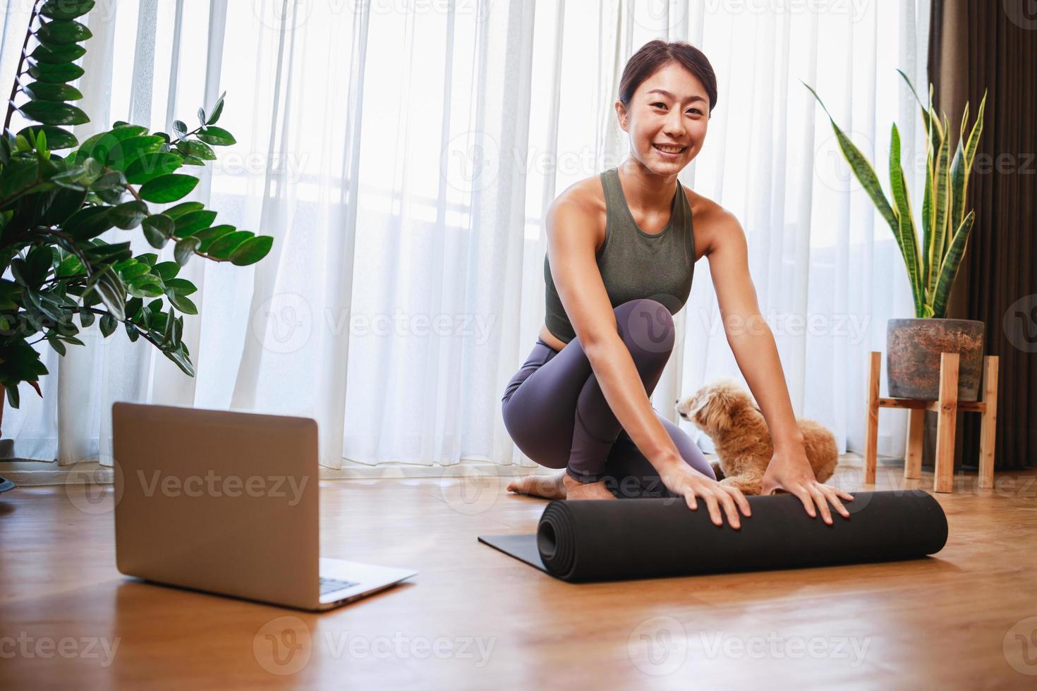 young Asian woman unrolling roll black yoga mat for online training yoga with her dog at home photo