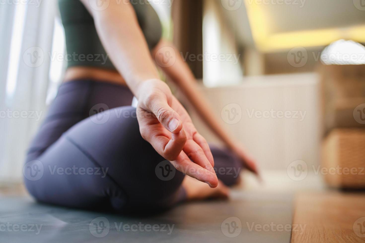 yoga, pose de loto cerca de la mujer de la mano mientras se sienta en la alfombra de yoga en la sala de estar en casa foto