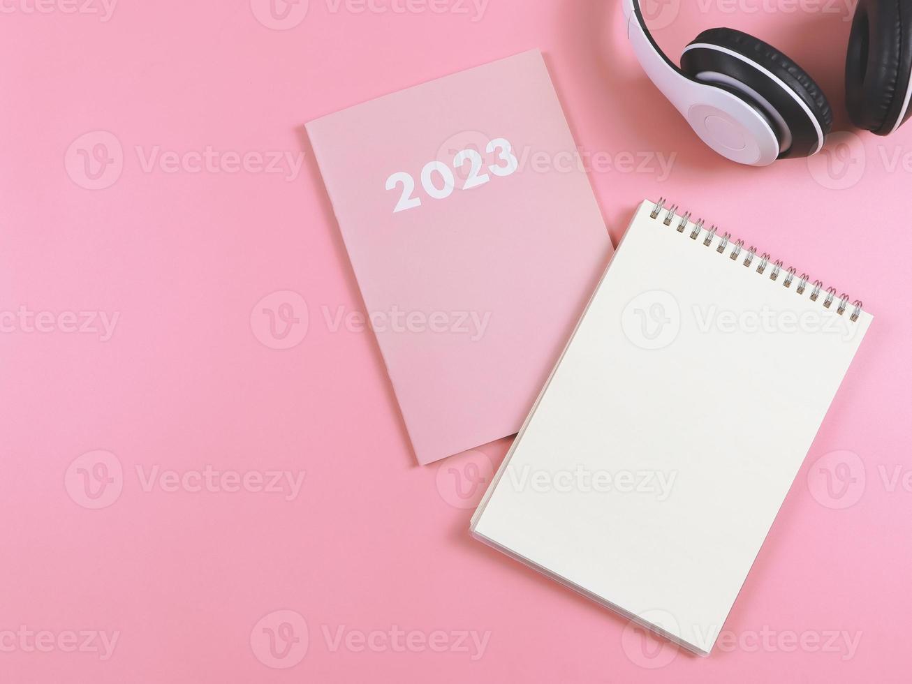 flat lay of blank paper note book on pink diary or planner 2023 and headphones  on pink  background with copy space. photo