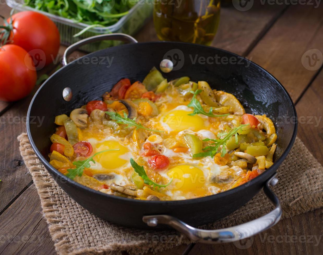 Fried eggs with vegetables in a frying pan on a wooden background photo