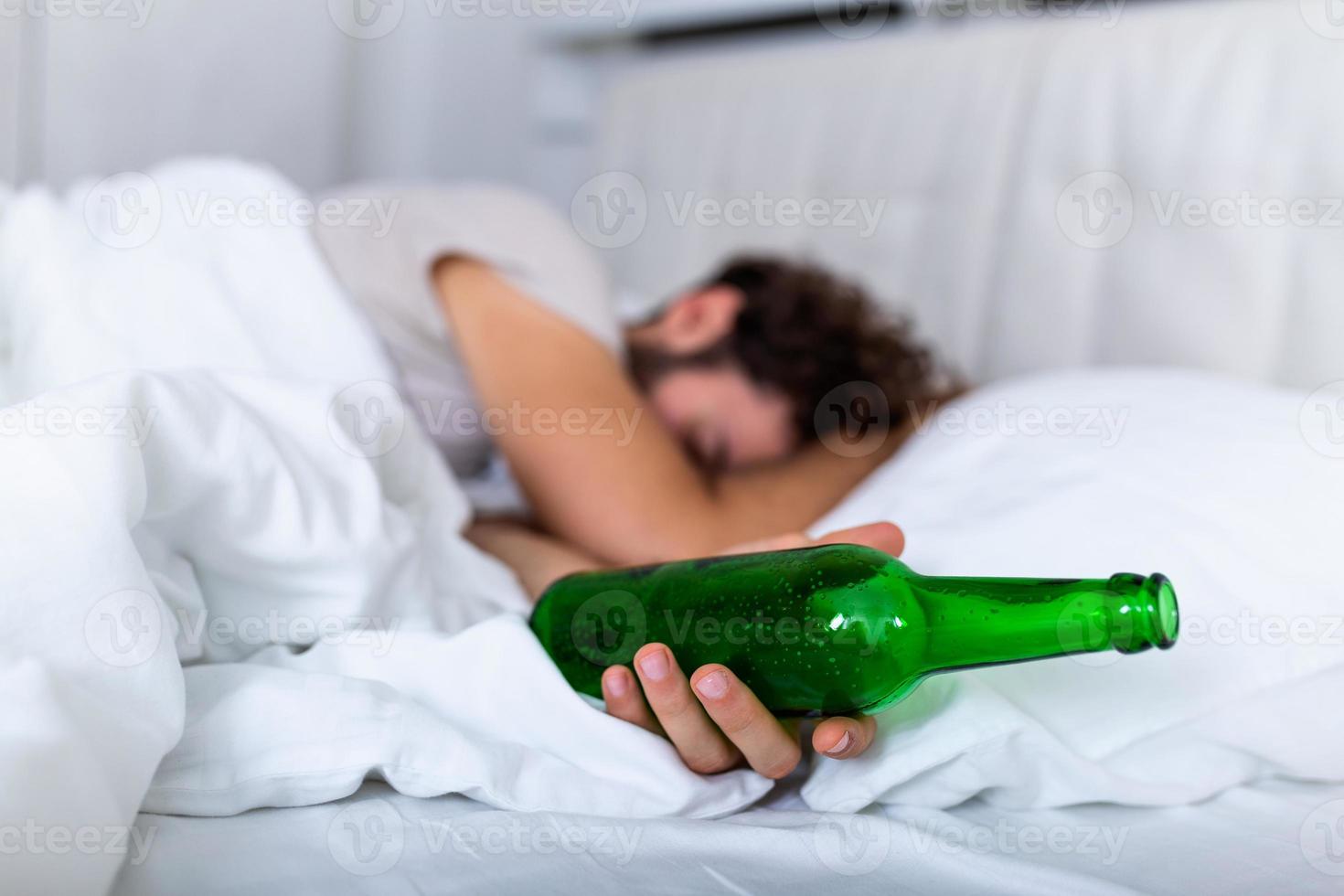 After drinking. Drunk bearded adult man lying on the bed and sleeping after drinking lots of alcohol, Empthy bottle on the bed, alcoholism, alcohol addiction and people concept photo