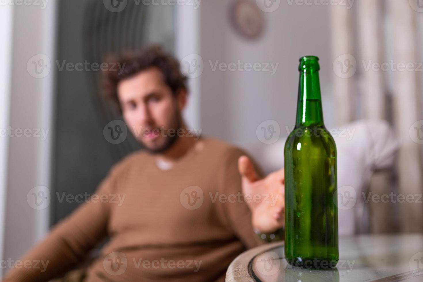 Alcoholic man reaching for bottle of beer, Man drinking home alone. alcoholism, alcohol addiction and people concept - male alcoholic with bottle of beer drinking at home alone photo