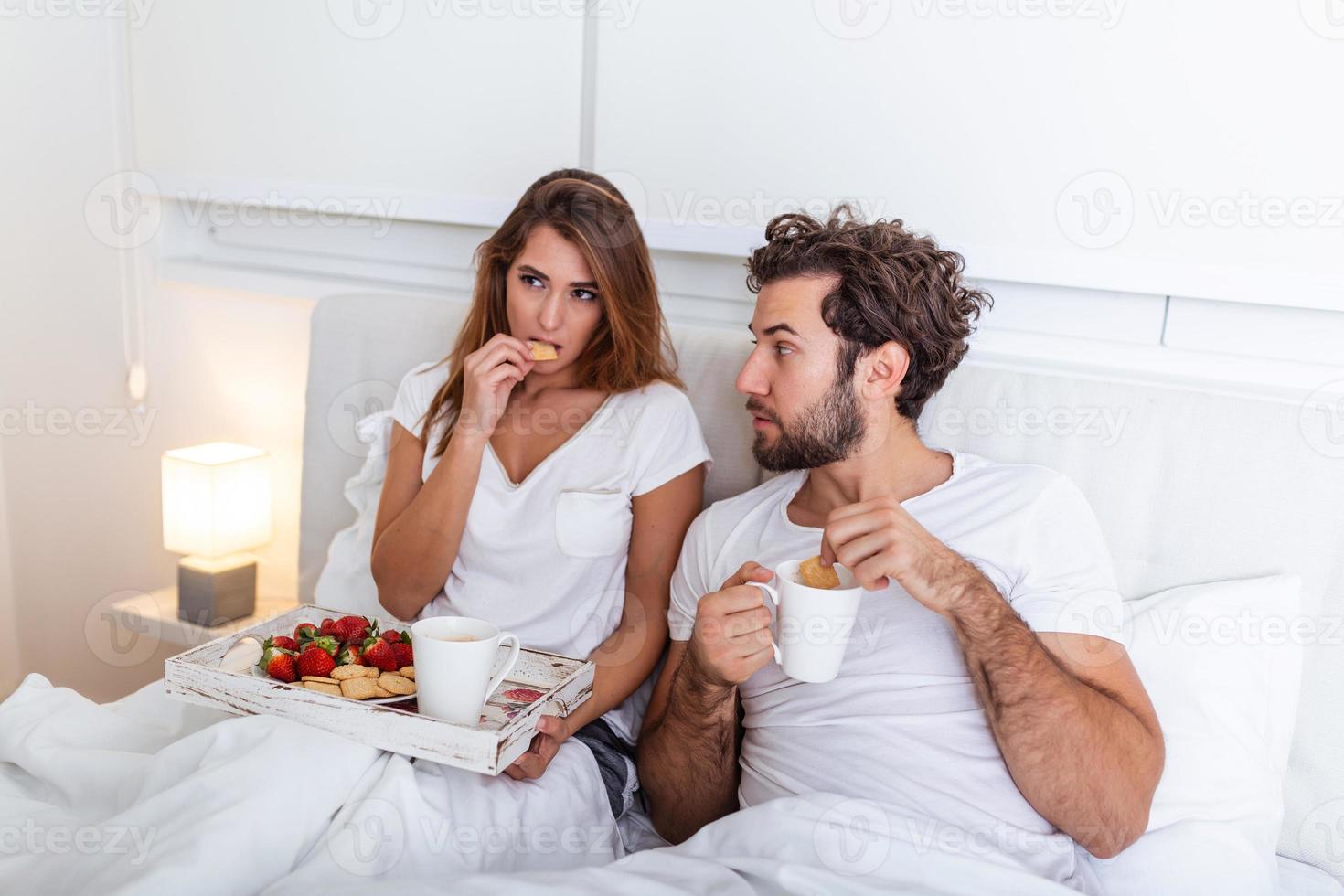 pareja enamorada desayunando en la cama. joven pareja caucásica desayunando romántico en la cama. hembra y macho, dos tazas de café, frutas y galletas coloridas. foto