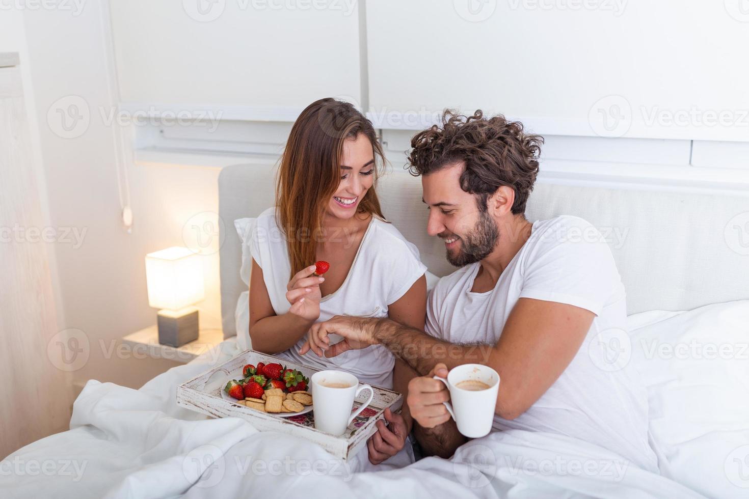 joven apuesto alimentando a una joven atractiva en la cama por la mañana. Desayuno romántico para dos. amor, cuidado, relaciones. pareja desayunando saludablemente en la cama en casa foto