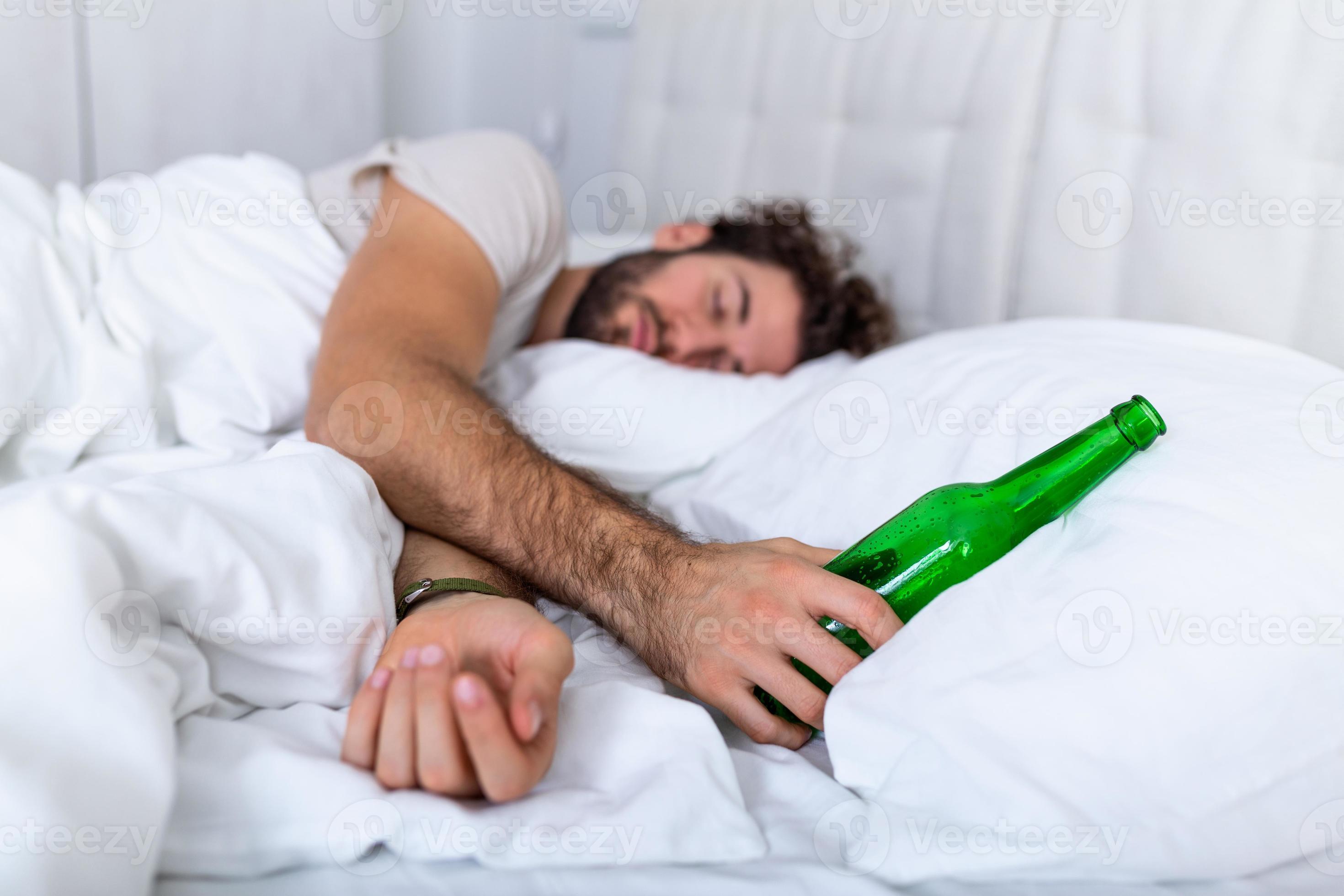 borracho en la cama y lugar triste y una botella de alcohol en la mano