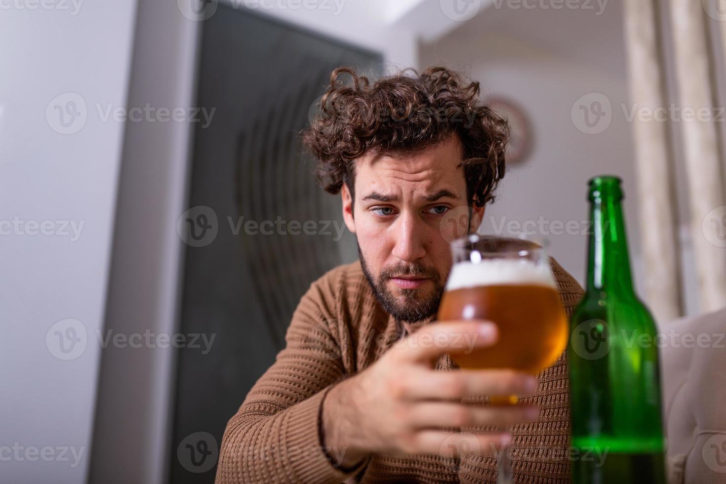 After work a depressed guy sitting on sofa, drinking a cold beer. Hand holding a glass, Man drinking home alone. alcoholism, alcohol addiction and people concept photo