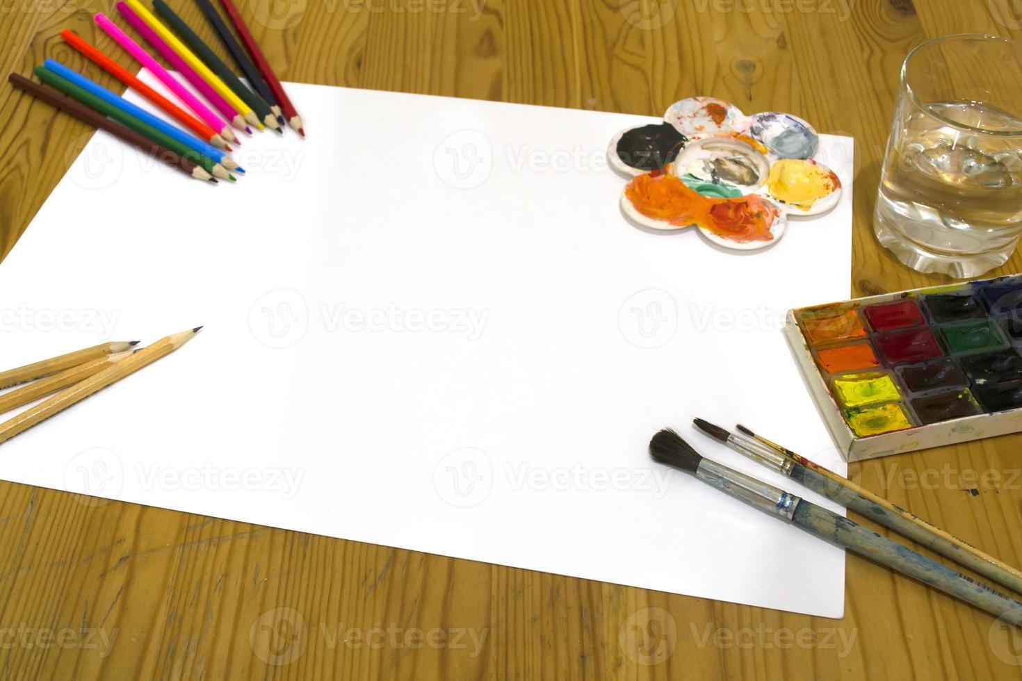 Drawing supplies. Pencils, paints, brushes, paper and a glass of water on the table. photo