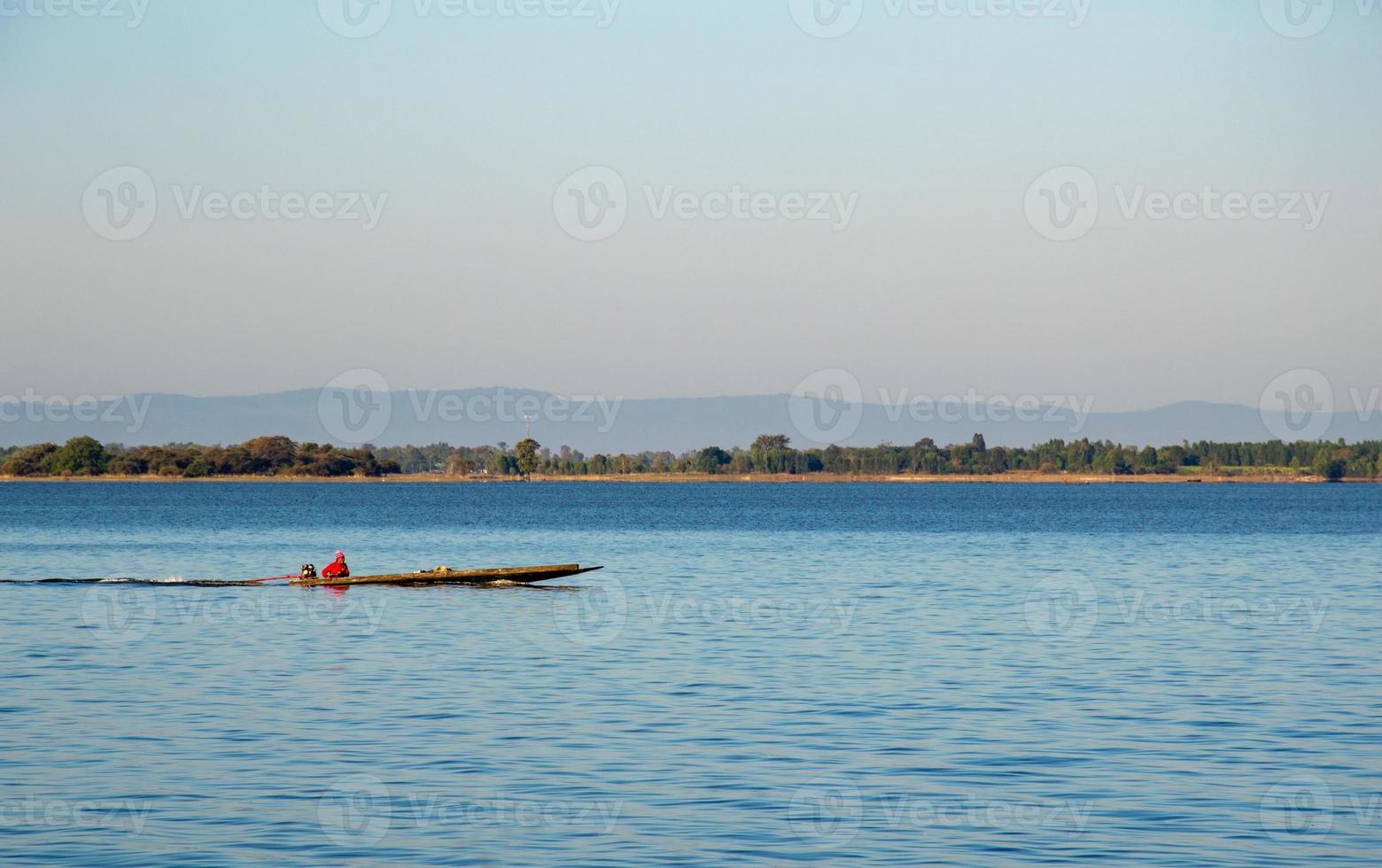 un pescador con una camisa roja conduce un bote en el río. fondo de bosque y montaña foto