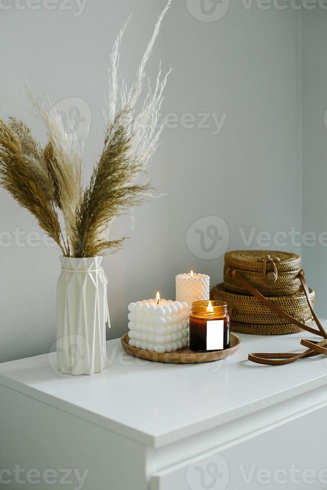 Home interior decor in beige neutral colors. White dresser with dried flowers in vase, rattan bags and candle. Mockup concept photo