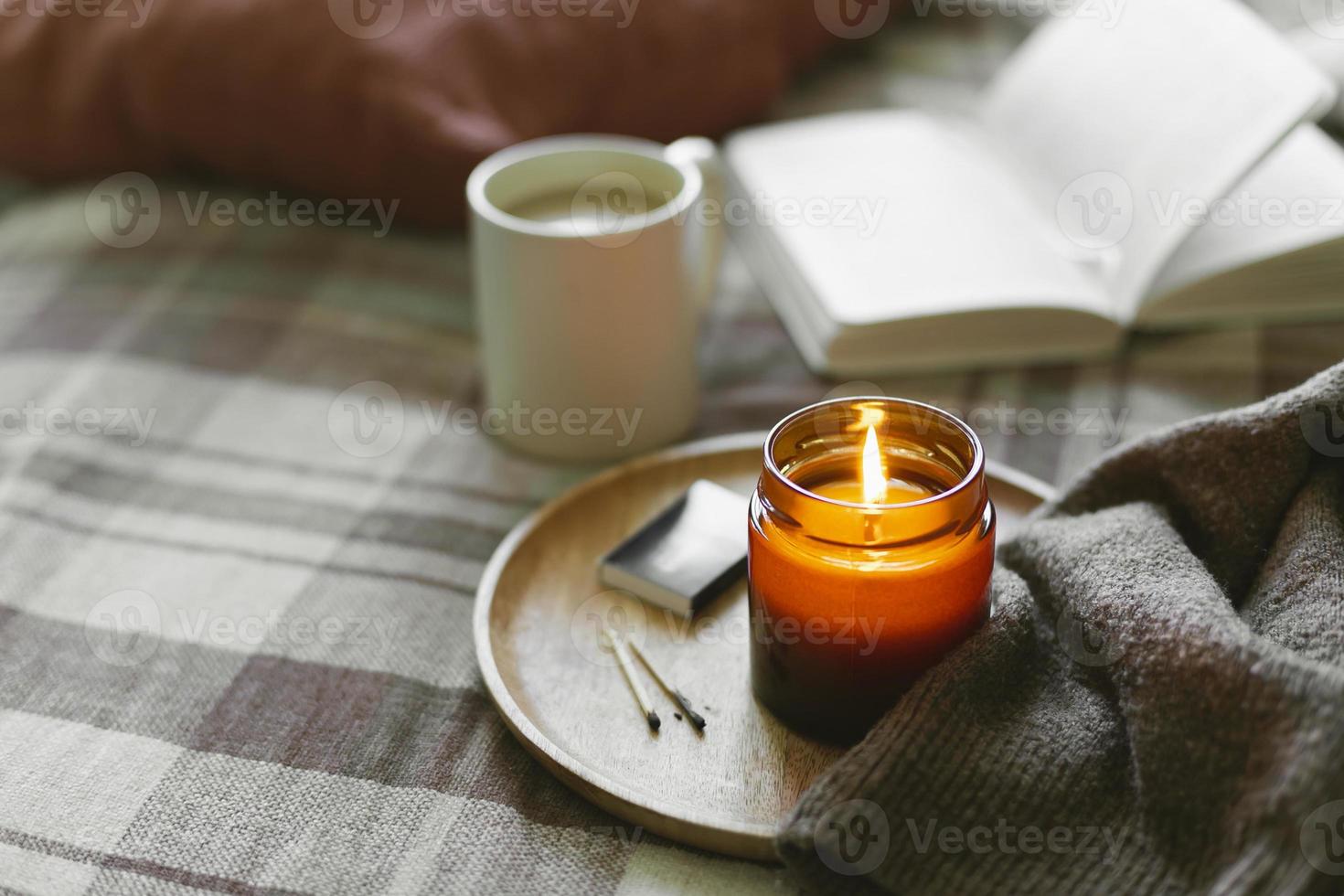 Burning candle with wooden wich in amber glass gar, open book and cup of coffee or tea. Autumn home decor. photo