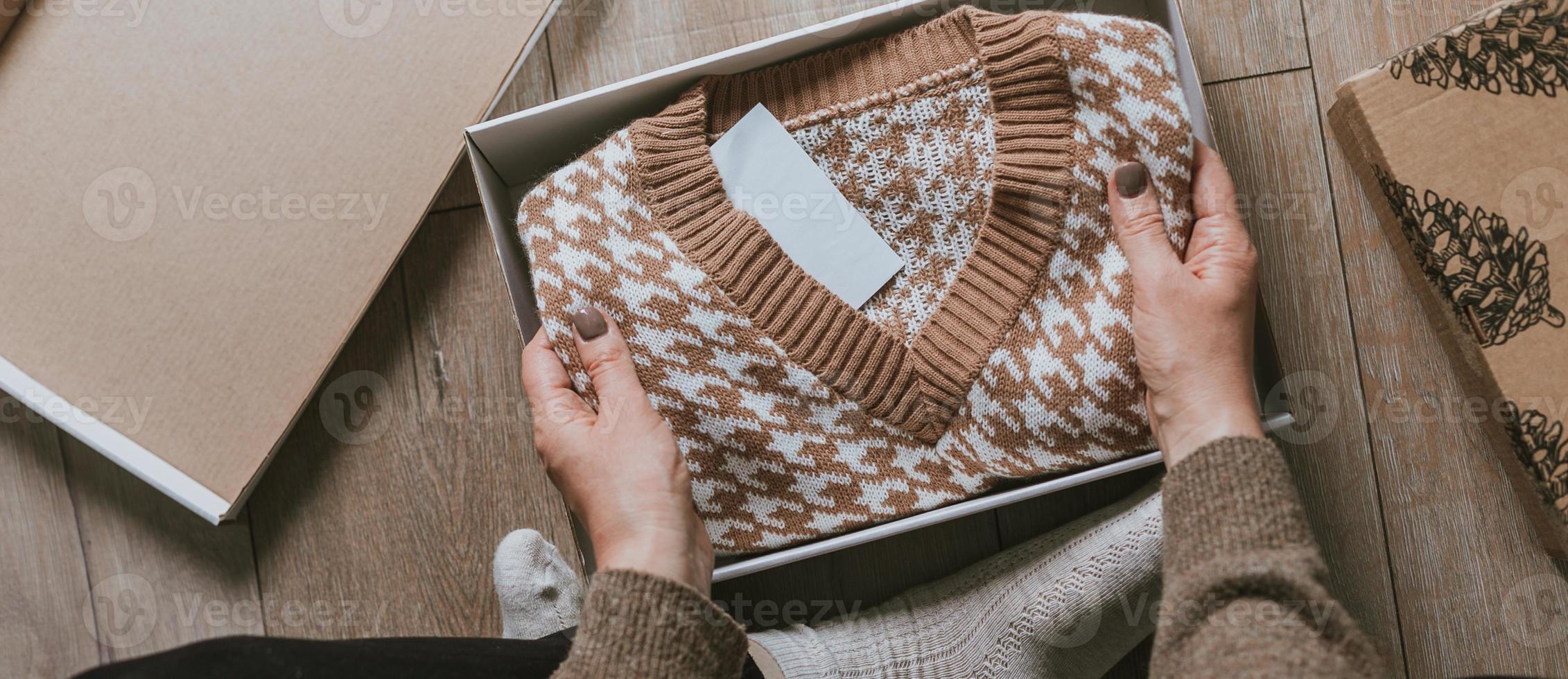 manos femeninas sosteniendo un suéter acogedor. concepto de compras en línea, desempacar regalo para navidad foto