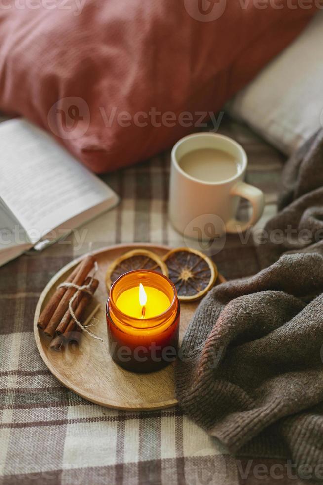 Burning candle with wooden wich in amber glass gar, open book and cup of coffee or tea. Autumn home decor. photo