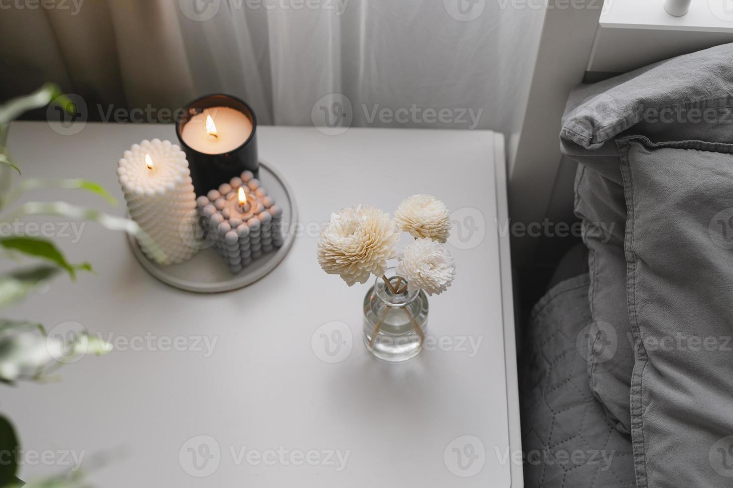 Aromatic reed air freshener and burning candle on bedside table in the bedroom. Home aroma. Wellness photo