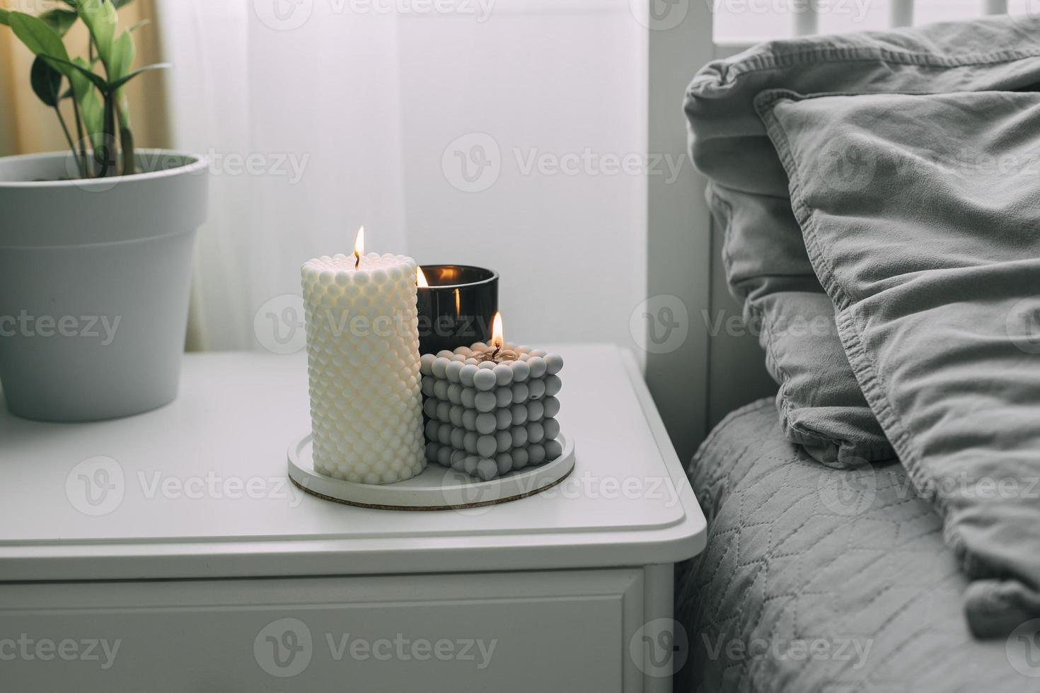 mesita de noche cerca de la cama en el dormitorio con velas encendidas. concepto de hogar acogedor aroma, bienestar foto