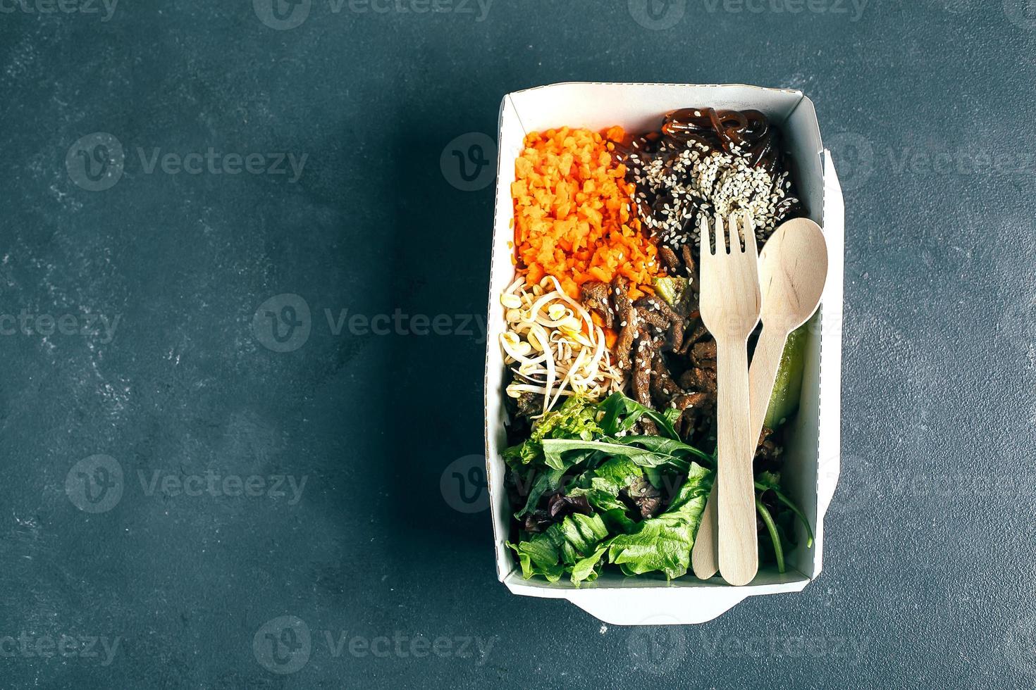 Reusable packaging container with asian lunch - beef, noodles, mix green leaves, sprouts, vegetables photo