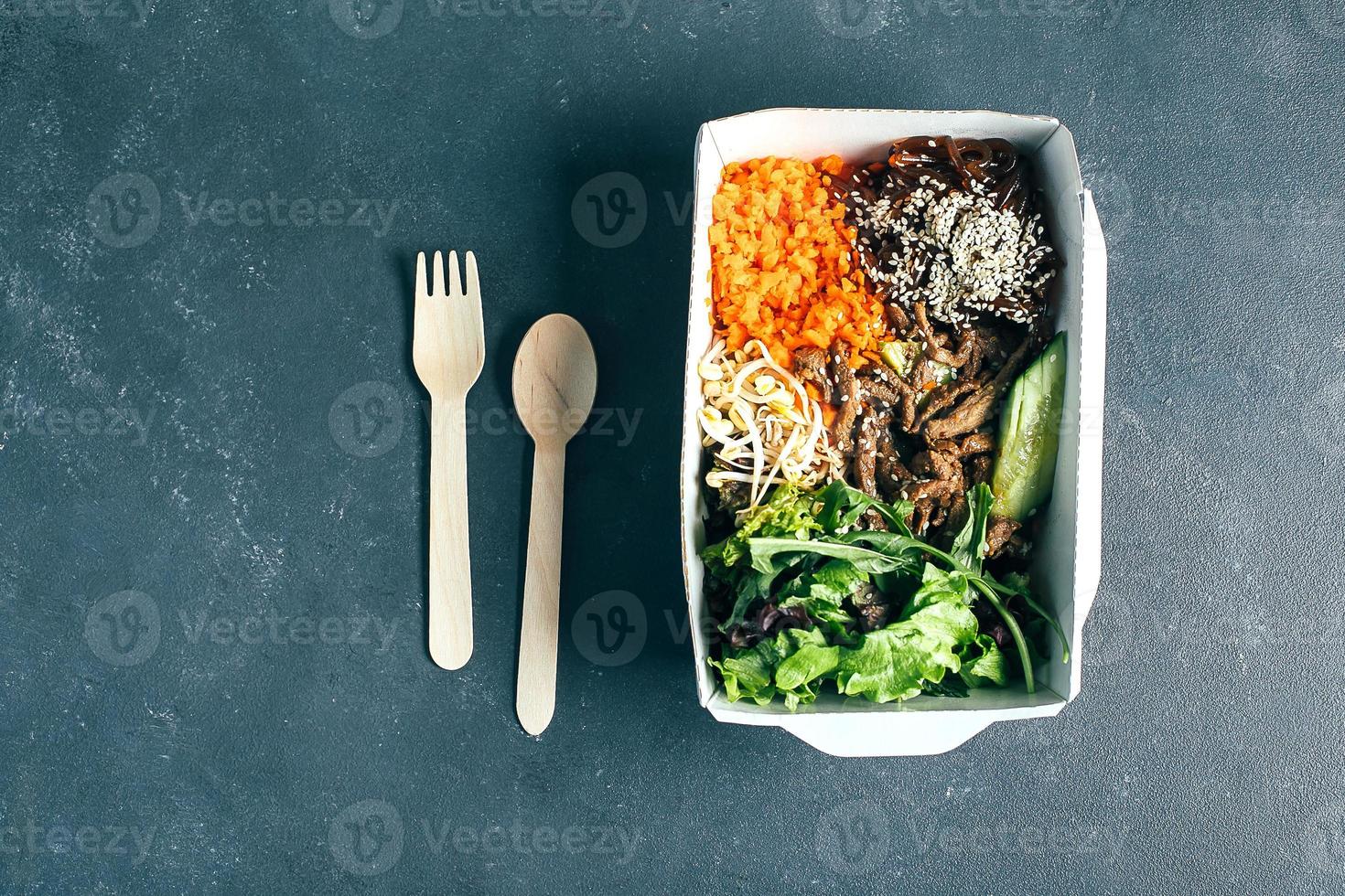 Reusable packaging container with asian lunch - beef, noodles, mix green leaves, sprouts, vegetables photo