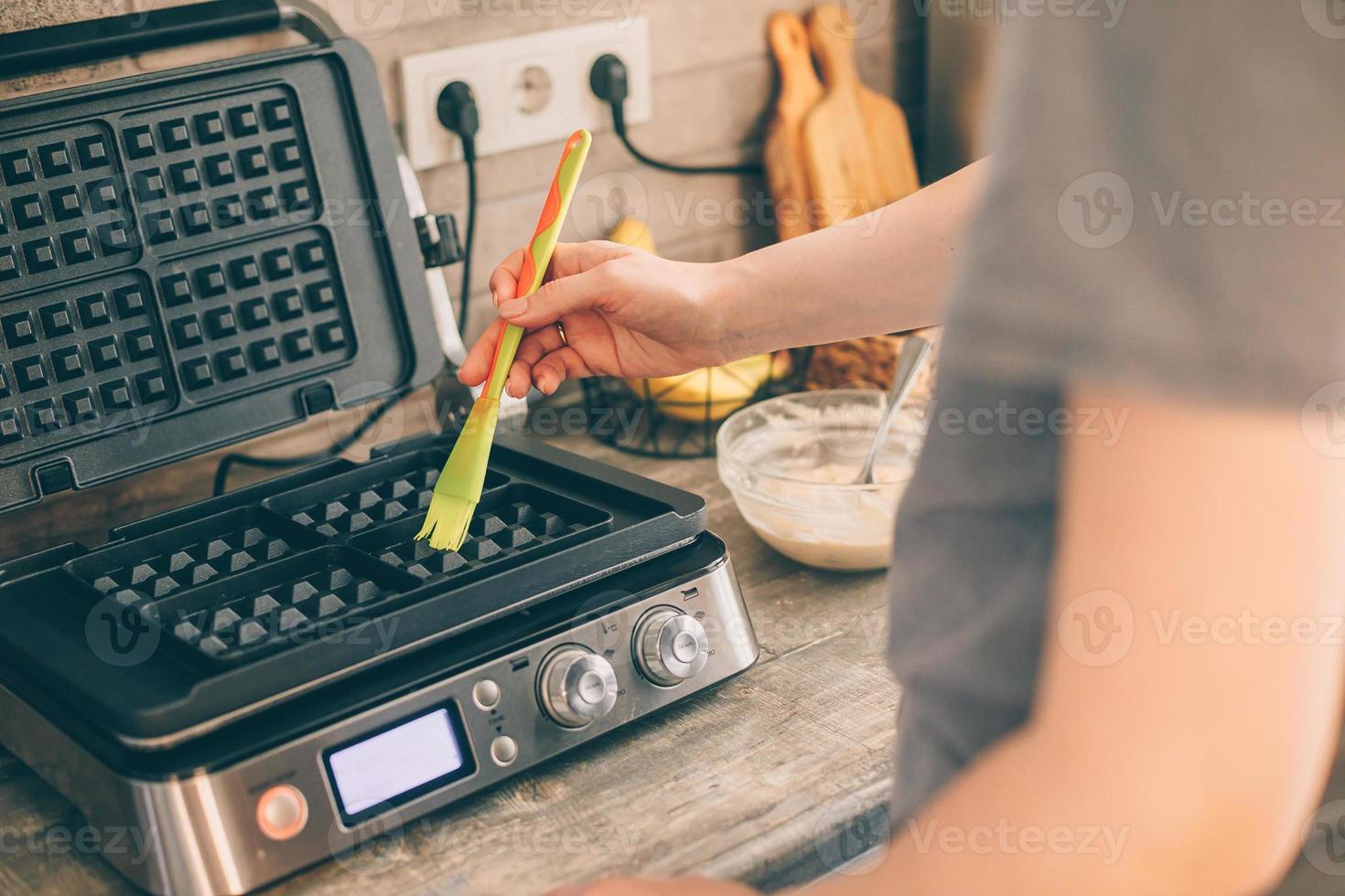 mujer joven preparando gofres belgas en la cocina, engrasando la plancha de gofres con aceite de coco. proceso de cocción foto