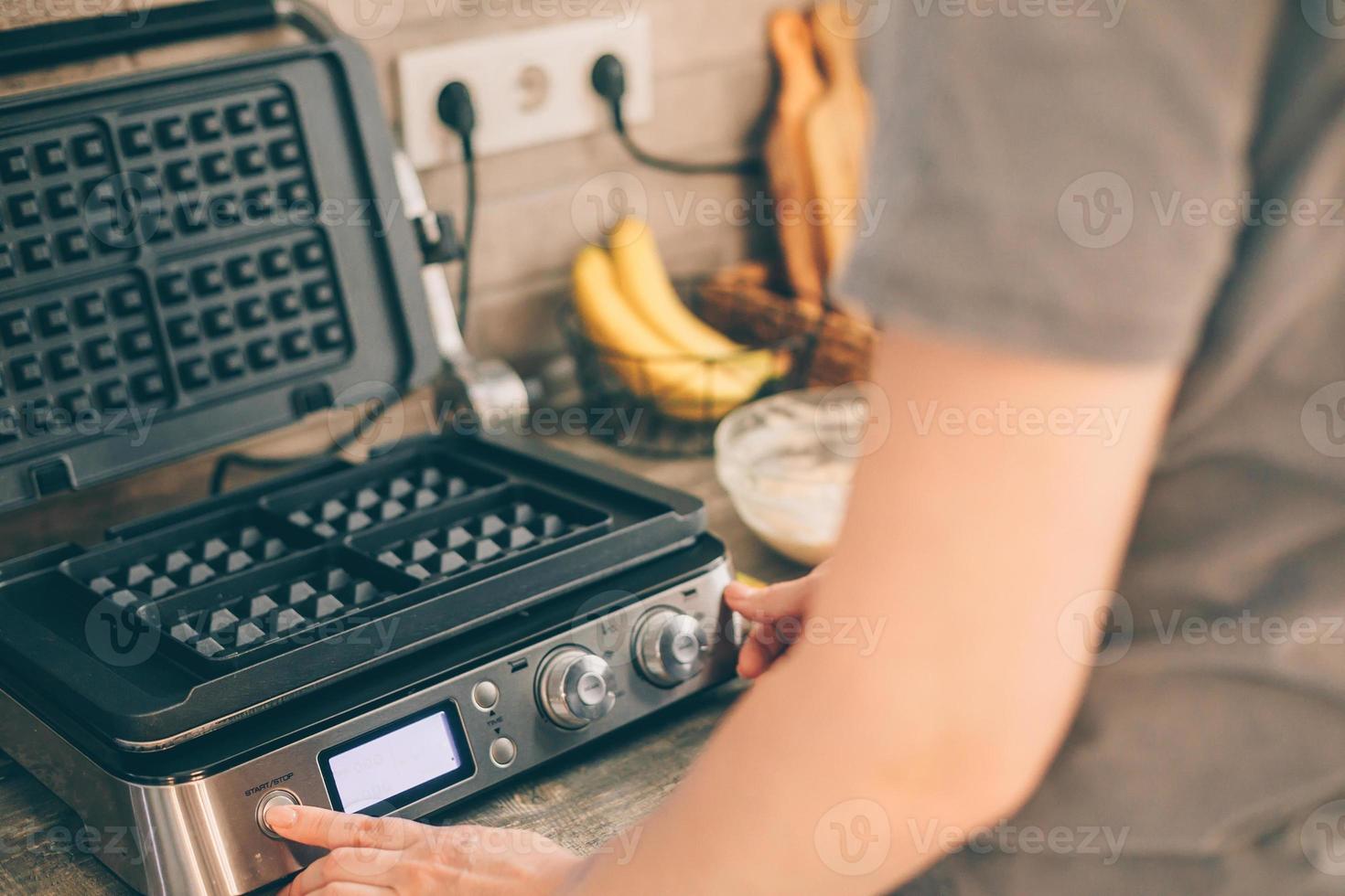 Young woman includes waffle iron, preparing Belgian waffles in the kitchen. Cooking process photo