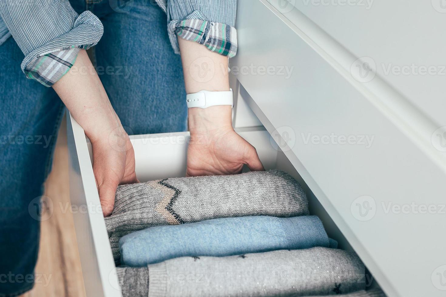 una mujer dobla suéteres de ropa en un cajón. concepto de almacenamiento de ropa, estilo de vida minimalista foto