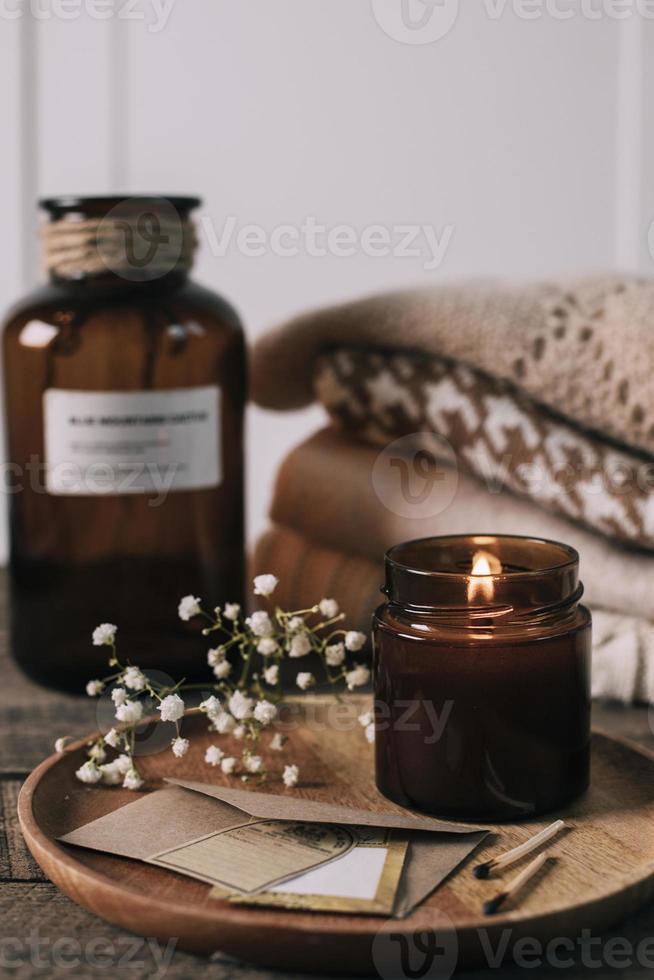 velas encendidas en un pequeño frasco de vidrio ámbar, flores de gypsophila y suéteres de punto apilados. estilo de vida acogedor, concepto hygge foto