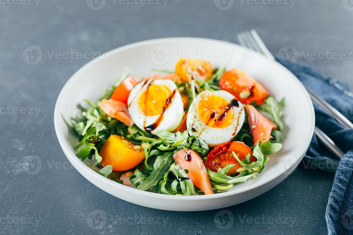 Healthy vegan salad of fresh tomato, arugula, salmon, egg and sesame on plate. Diet menu. Close-up photo