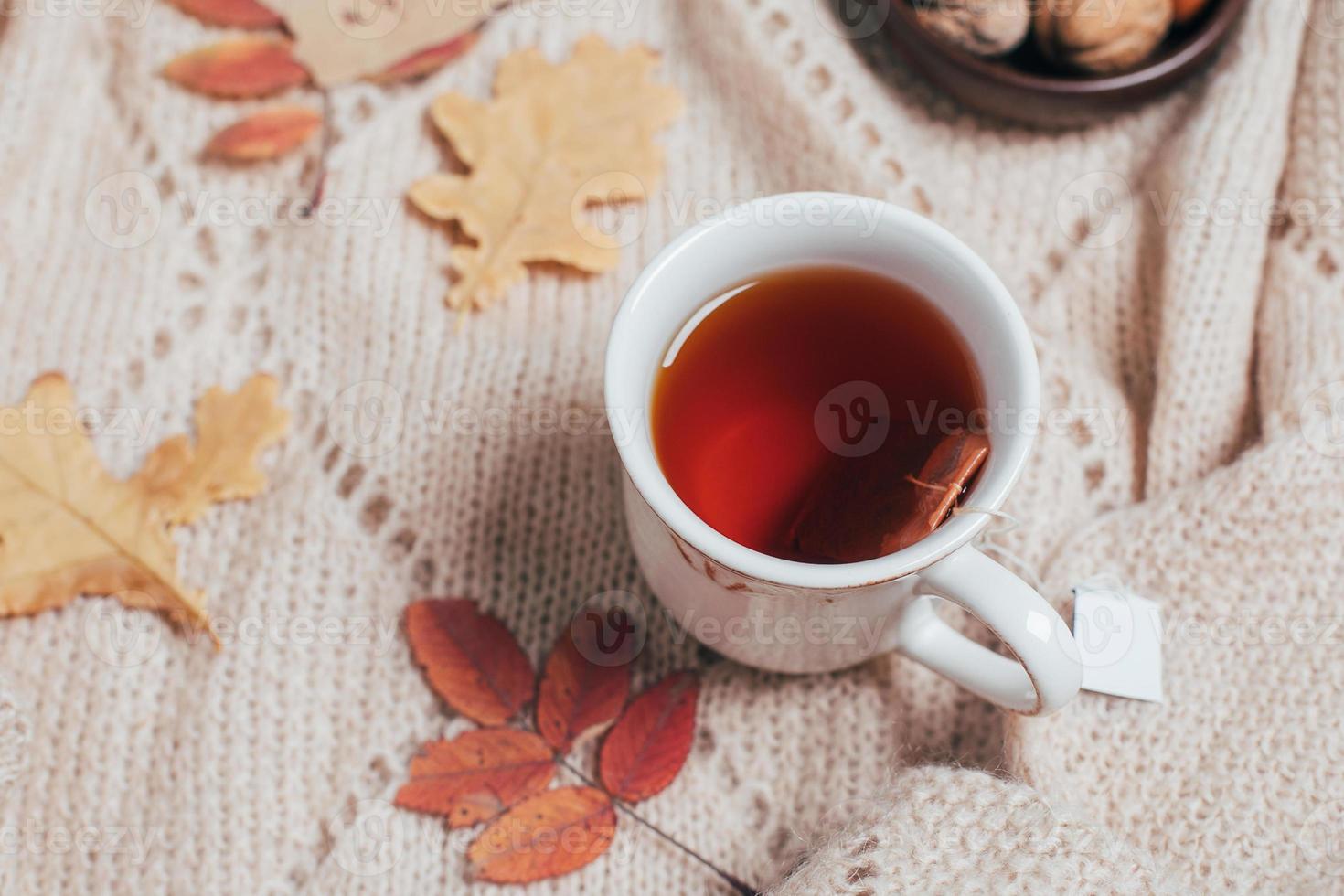 taza de té caliente, hojas de otoño en una acogedora tela escocesa beige. concepto de bebida caliente. foto