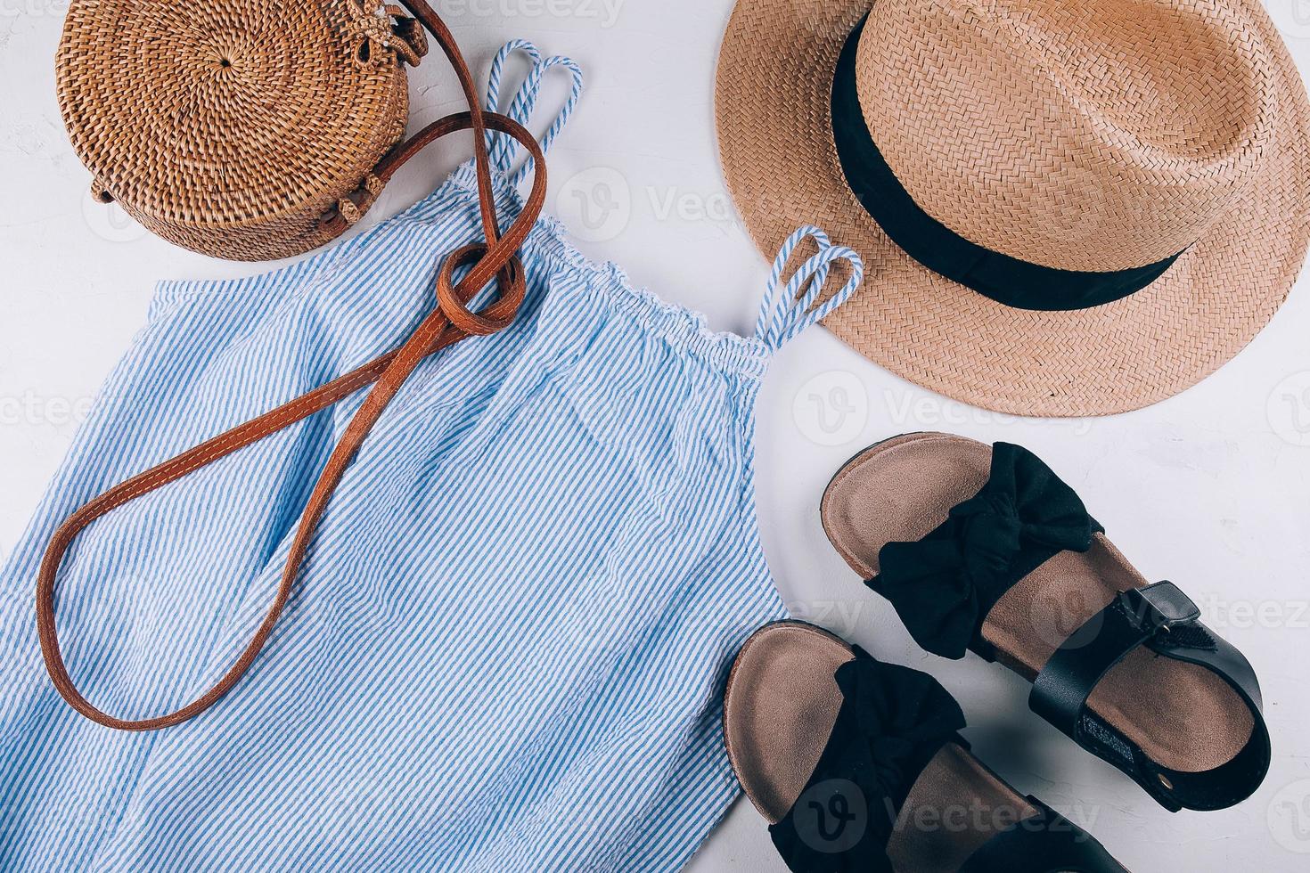 Women's fashion flat lay. Stylish female clothes - straw hat, blue dress, rattan bag, sandals. photo