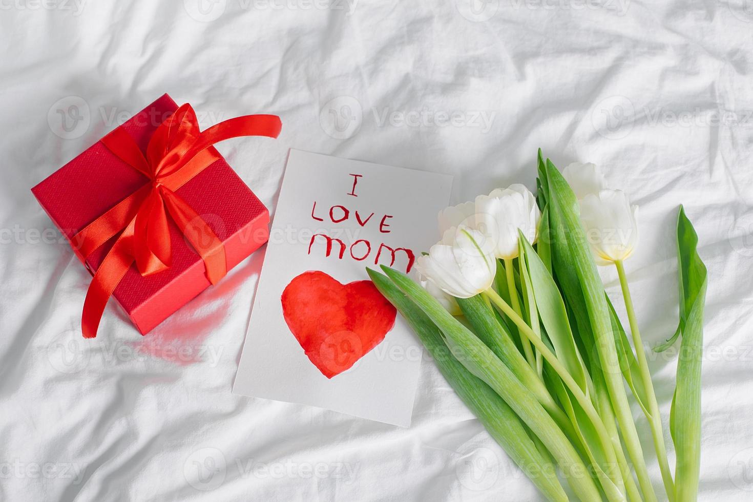 flores de tulipanes, caja de regalo roja y tarjeta con texto amo a mamá. concepto del día de la mujer, día de la madre foto