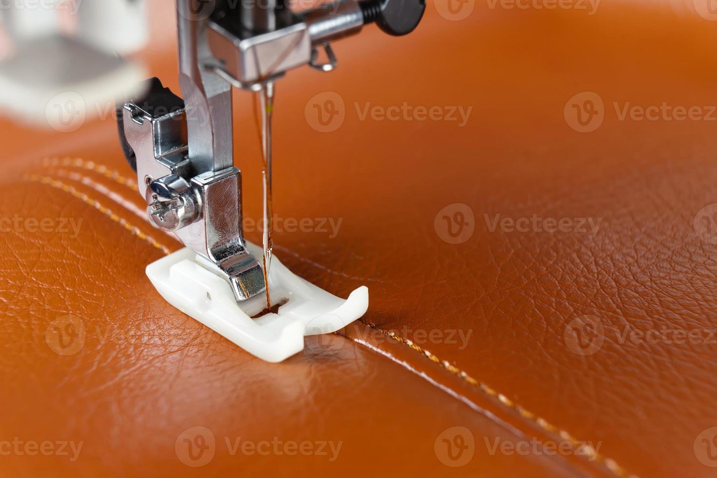 Modern sewing machine presser foot with a needle sews brown leather photo