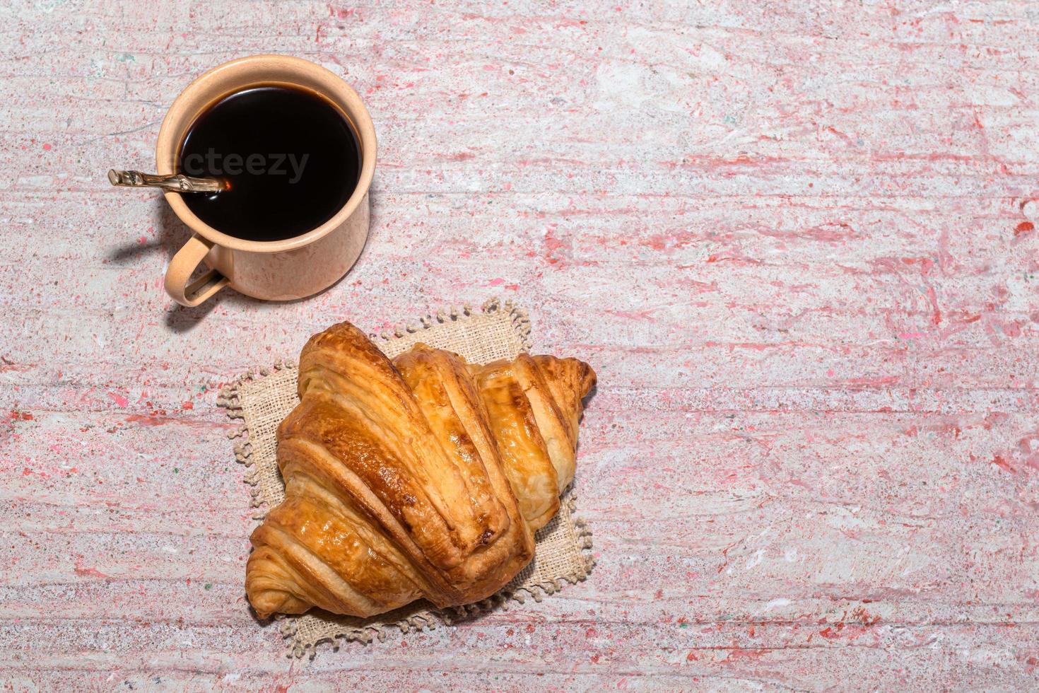 Breakfast food croissant in cutting board and coffee on red wood table. photo