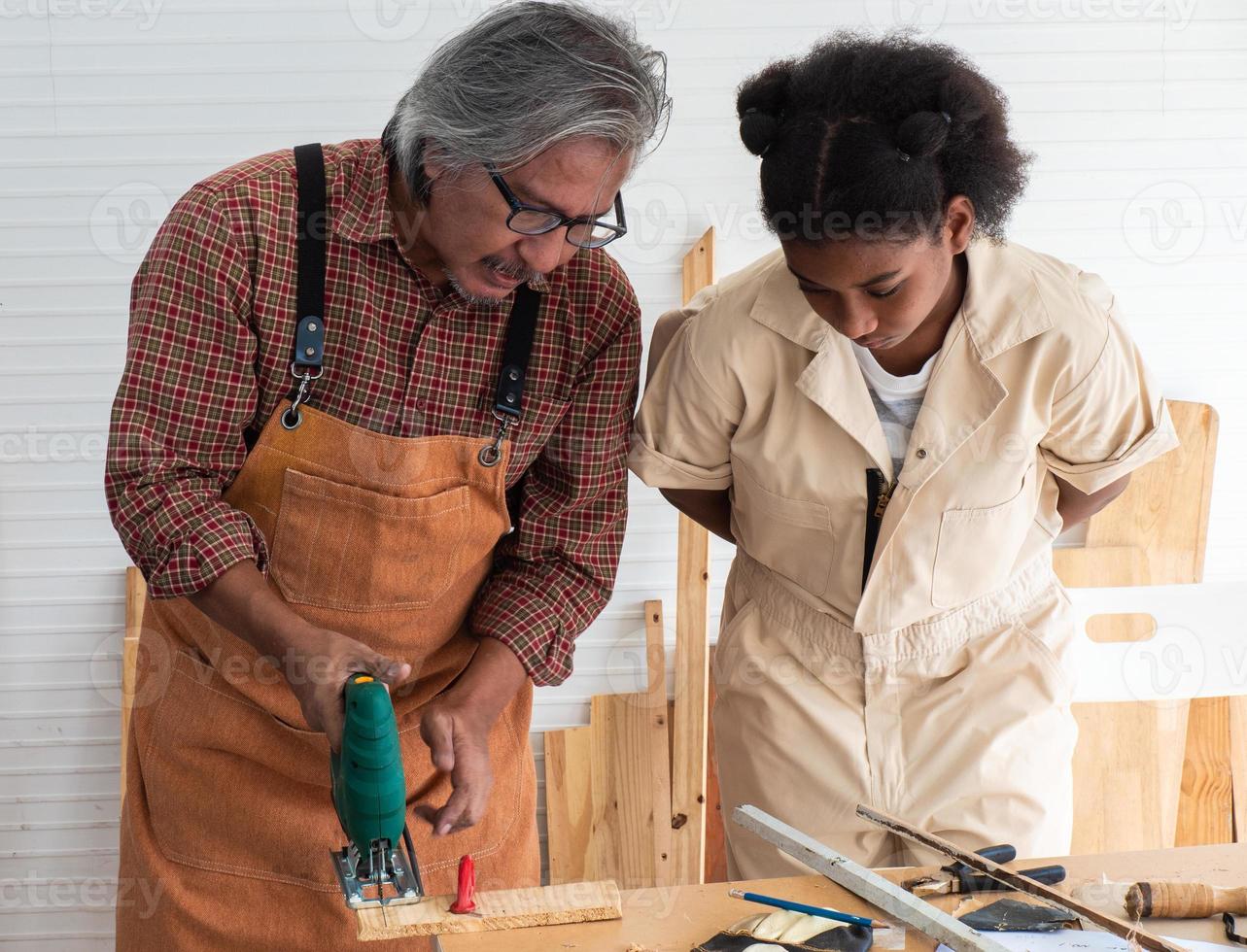Teenaged girls learn to use an electronic saw and play with their grandfather in the wooden workshop, a concept for enhancing the development and thinking of children. photo