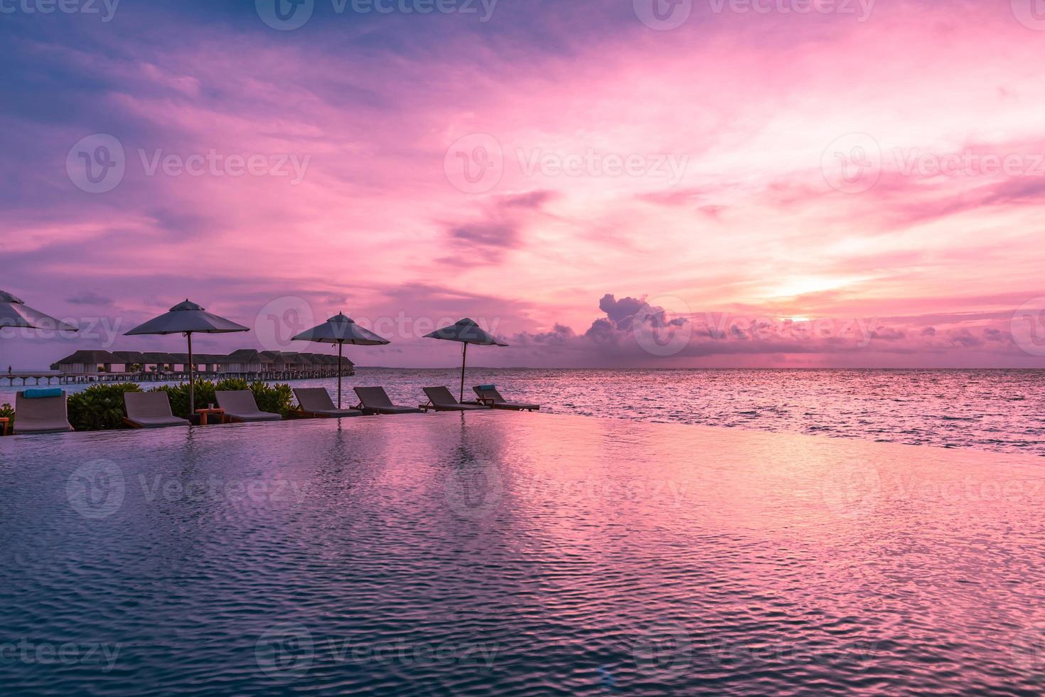 sombrilla y silla alrededor de la piscina infinita cerca de la playa del océano al amanecer o al atardecer. para viajes de ocio y concepto de vacaciones, paisaje de veraneo. vacaciones de relajación tropical, puesta de sol foto