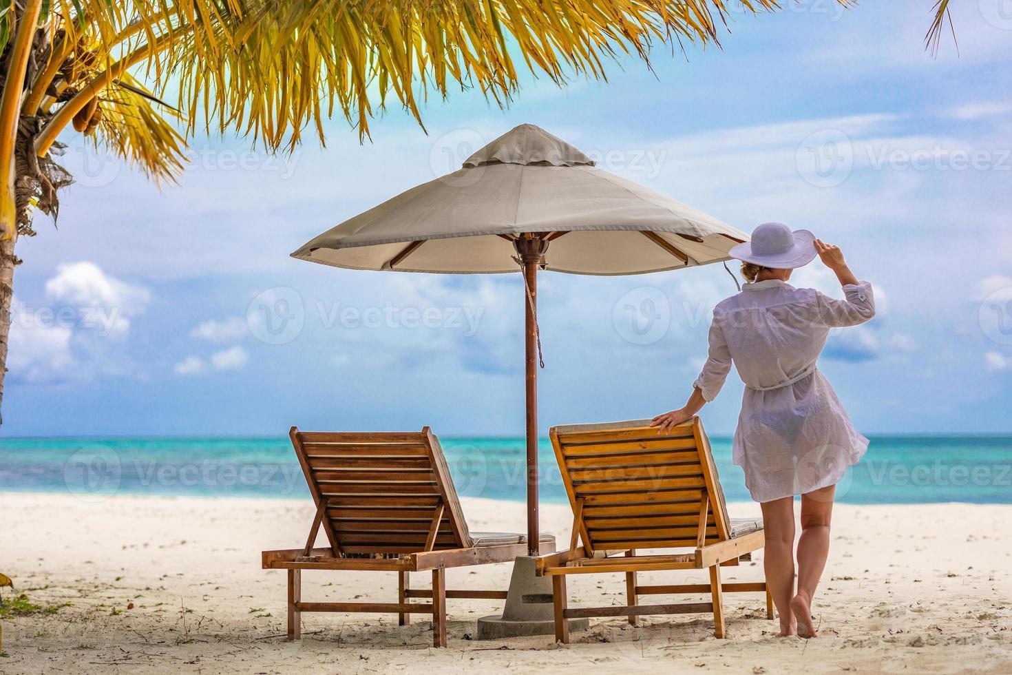 Summer young woman standing backwards and watching beach in white dress, hat. Summer beach colors with girl back view. Summer vacation beach tropical landscape. Bright summer scene, tranquility photo