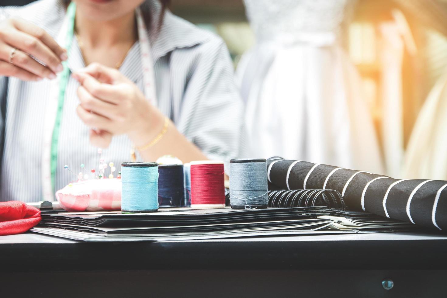 jóvenes empresarias, la propietaria de una pequeña tienda de ropa está sentada en un diseño de moda en el escritorio con equipo de costura. idea de negocio de inicio foto