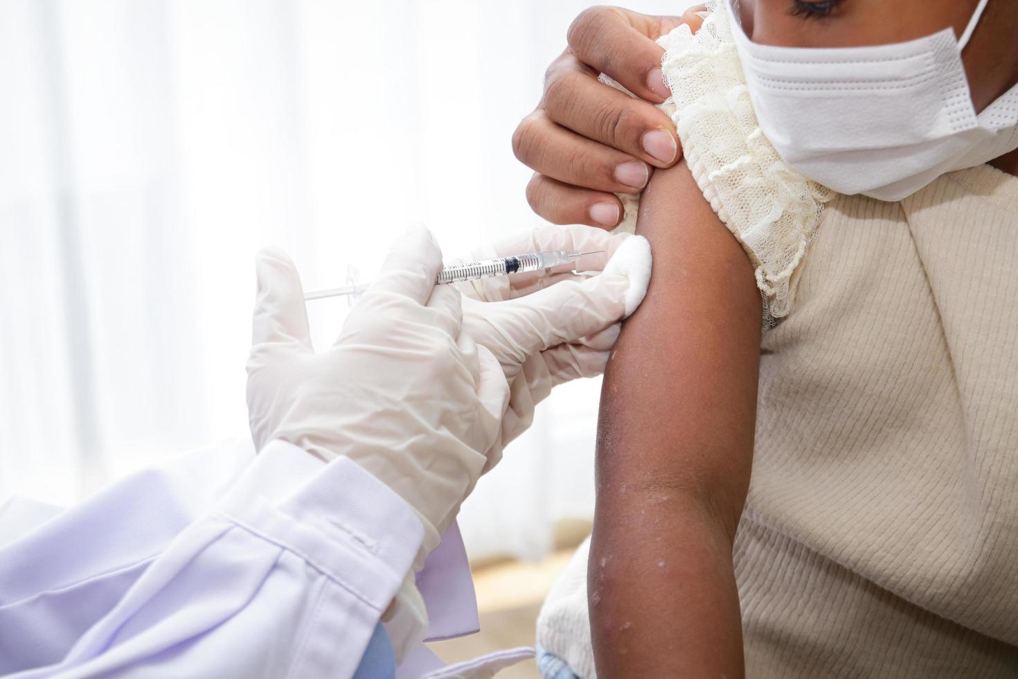 Doctors inject a vaccine in the arm of a young African-American girl to strengthen immunity and protect it from diseases. Concept of the vaccine against COVID-19. Medical services in hospitals. photo