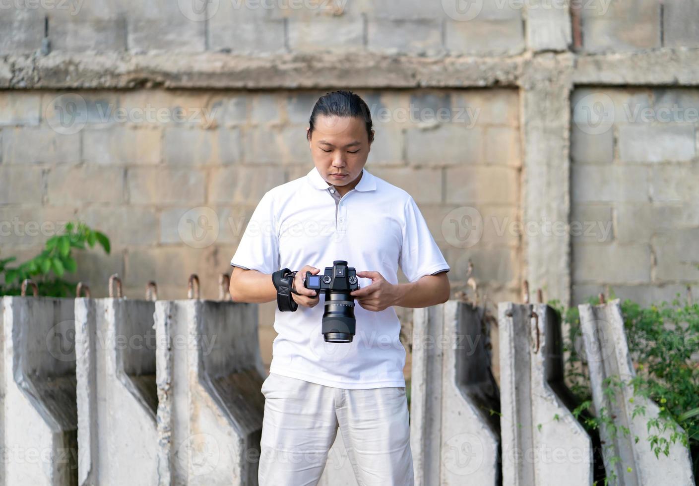 Asian Thai - Chinese professional camera man posts and check image shot via liveview behind Medium format Mirrorless camera with construction background. photo