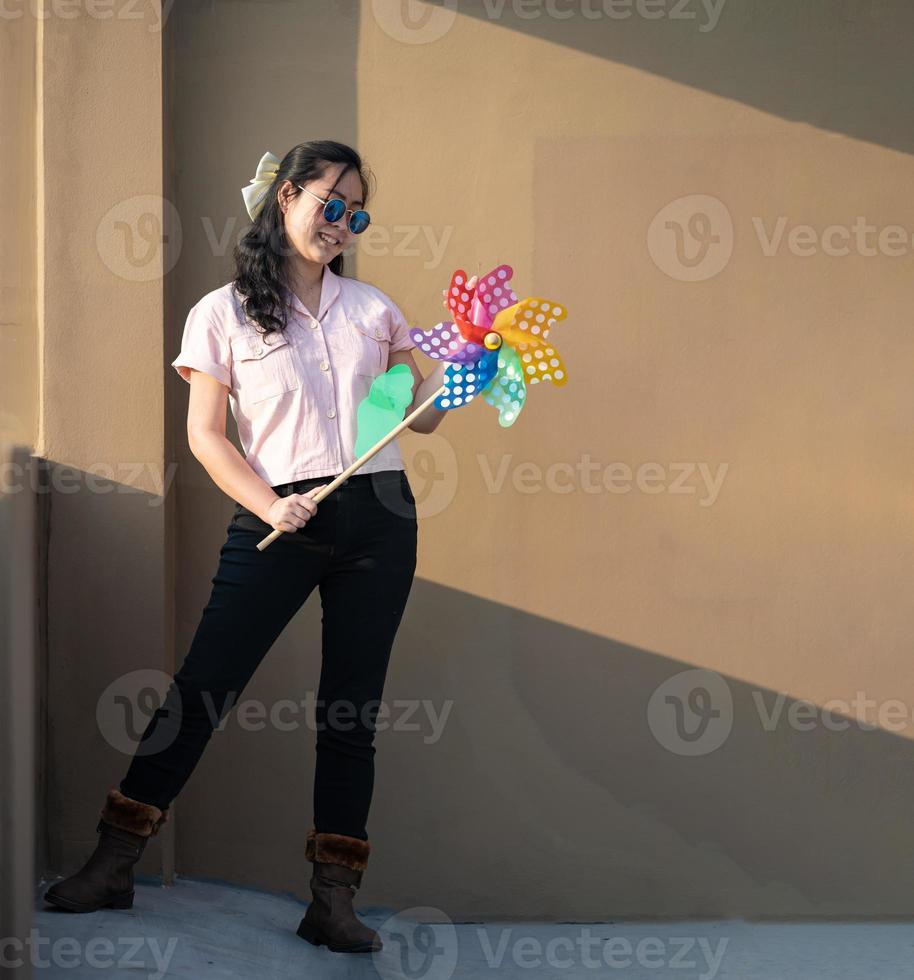 una mujer asiática publica y juega un juguete de molino de viento con el colorido arco iris en la azotea del edificio al atardecer. foto