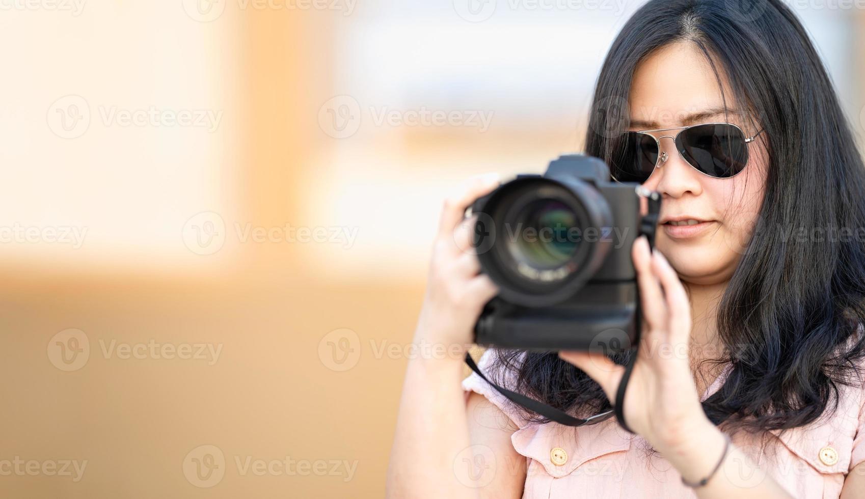 gafas de sol amateur mujer asiática toma una foto con una cámara profesional sin espejo en el edificio de la azotea azul al aire libre en el crepúsculo.