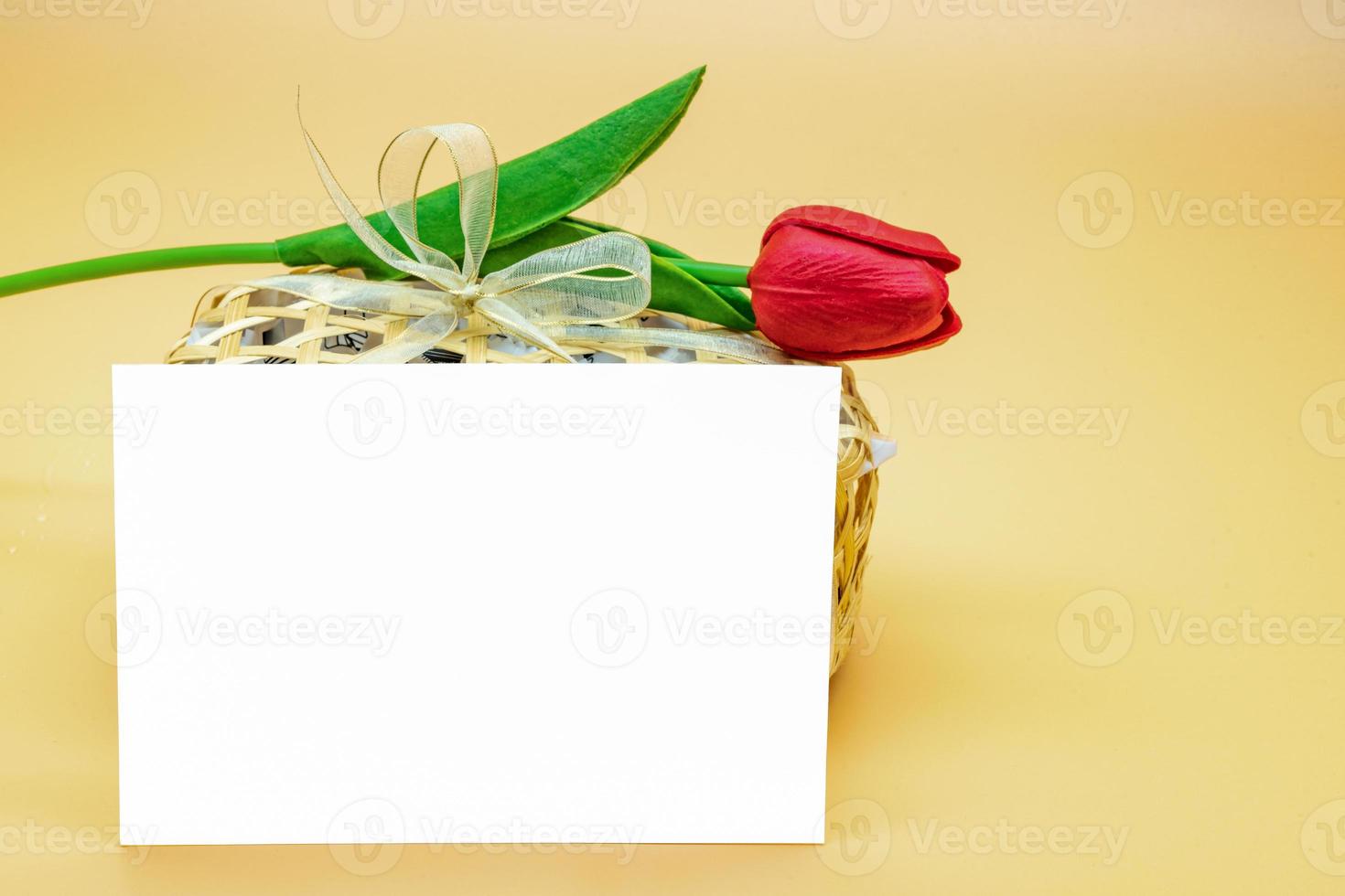 Empty Card in front of snack package and artifact red tulip on top of it on the cream - orange background. photo